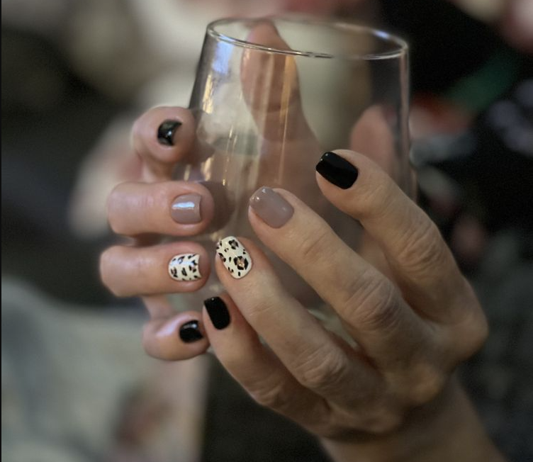 Hand holding a glass showing off a sophisticated nail design with black polish and leopard print on accent nails.