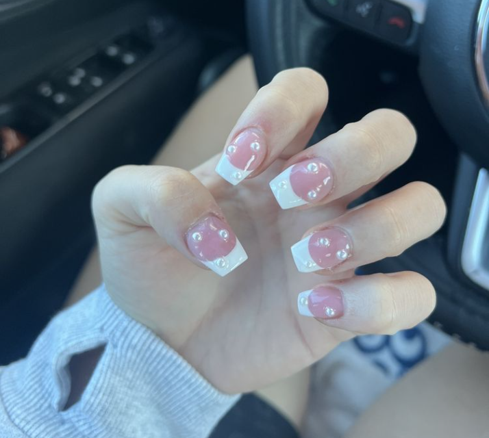 Close-up of a hand displaying a French manicure with pearl accents on pink nail beds and white tips.