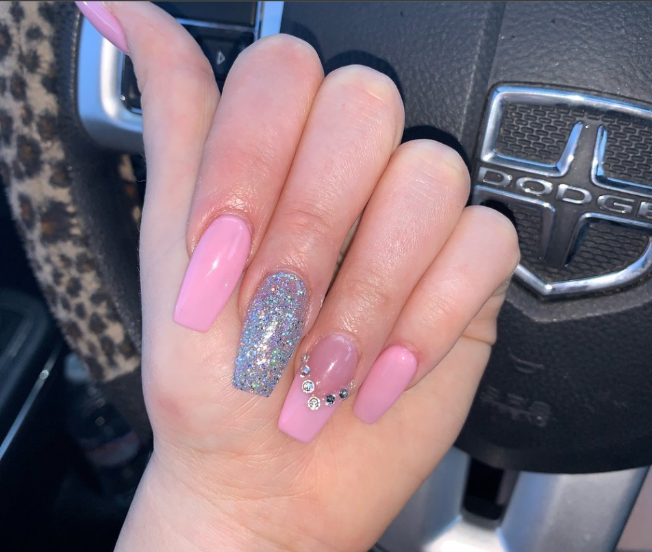 Hand displaying a nail design featuring pink polish and a silver glitter accent nail, with small gemstones for extra sparkle.